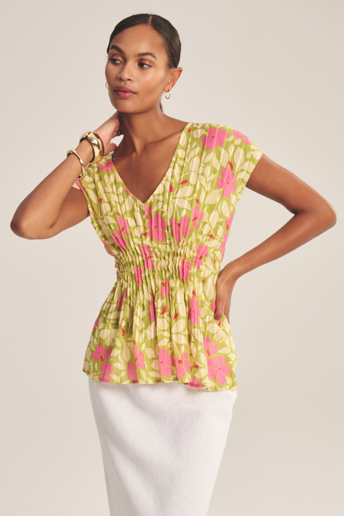 A woman wears the SARAH TOP by Velvet by Graham & Spencer—a short-sleeve, V-neck cotton top with a yellow, green, and pink floral pattern and subtle Lurex detailing—paired with a white skirt.
