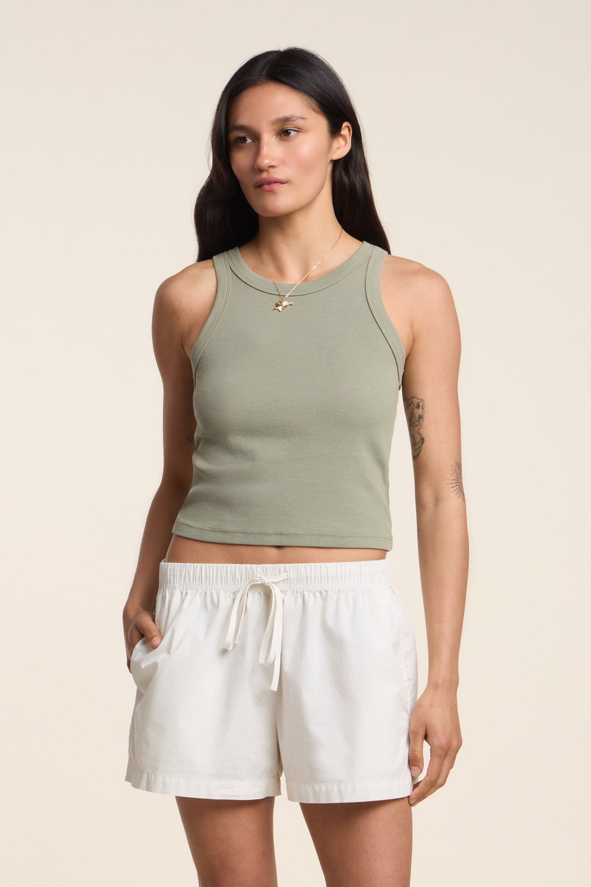 A woman with long dark hair wears the Velvet by Graham & Spencer SARI TANK TOP in light green with white drawstring shorts, standing against a plain beige background.