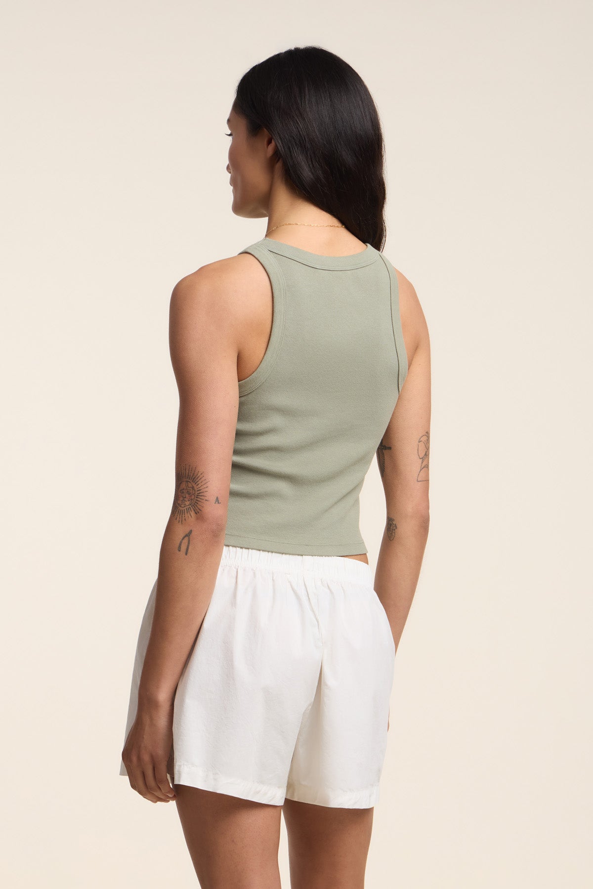 A person with long dark hair wears the Velvet by Graham & Spencer SARI TANK TOP in sage green, paired with white shorts, standing against a plain background—a true modern essential.-41645099483329
