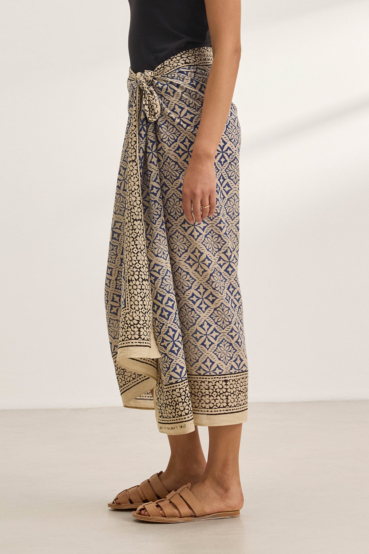   A person stands indoors on a light floor, wearing the JENNA SARONG by Velvet by Graham & Spencer and sandals. 