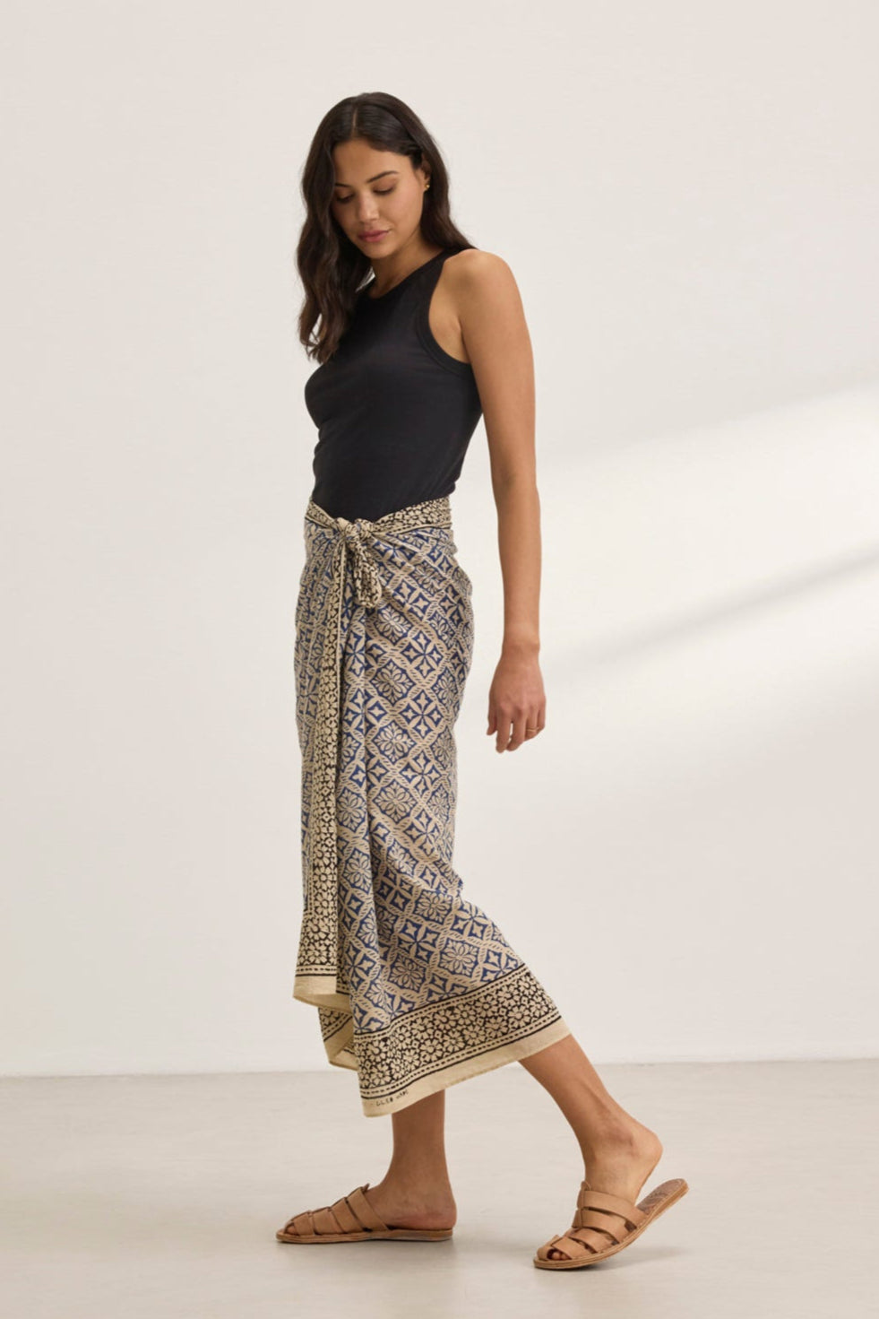   A person in a black tank top and vibrant Velvet by Graham & Spencer JENNA SARONG is standing on a light-colored floor, paired with brown sandals. 