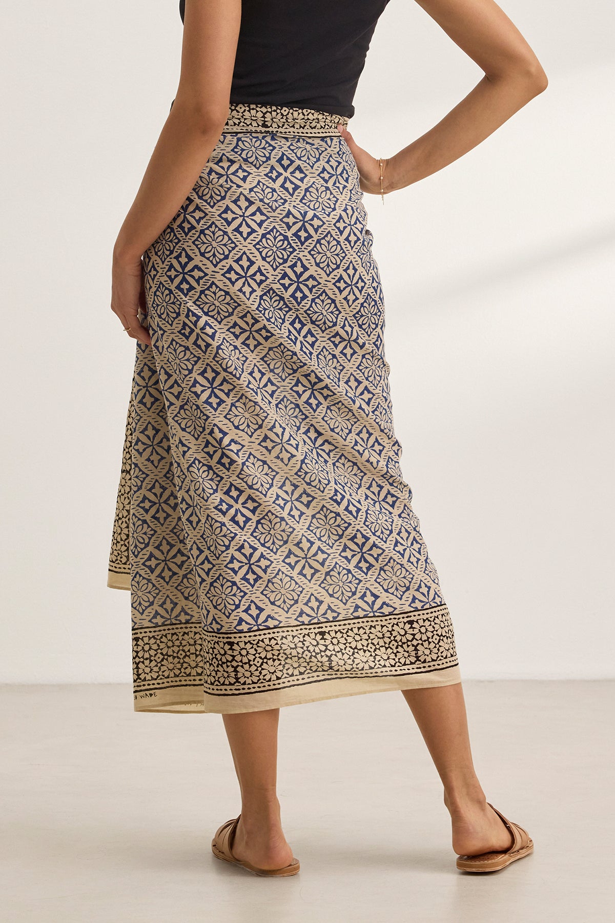   Against a plain background, a person wears the JENNA SARONG, featuring geometric designs reminiscent of a classic sarong, paired with a black top from Velvet by Graham & Spencer. 