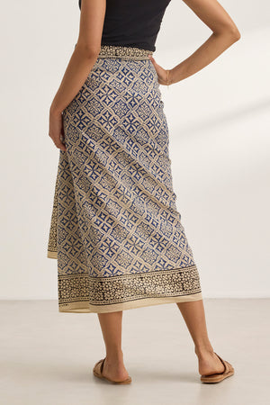 Against a plain background, a person wears the JENNA SARONG, featuring geometric designs reminiscent of a classic sarong, paired with a black top from Velvet by Graham & Spencer.