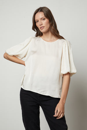 The model is wearing a DESI SATIN PUFF SLEEVE TOP by Velvet by Graham & Spencer.