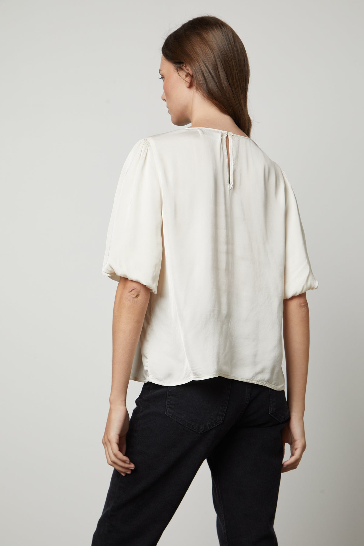   The back view of a woman wearing a DESI SATIN PUFF SLEEVE TOP blouse by Velvet by Graham & Spencer. 