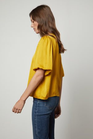 The back view of a woman wearing a Velvet by Graham & Spencer relaxed fit yellow blouse with DESI SATIN PUFF SLEEVE TOP.