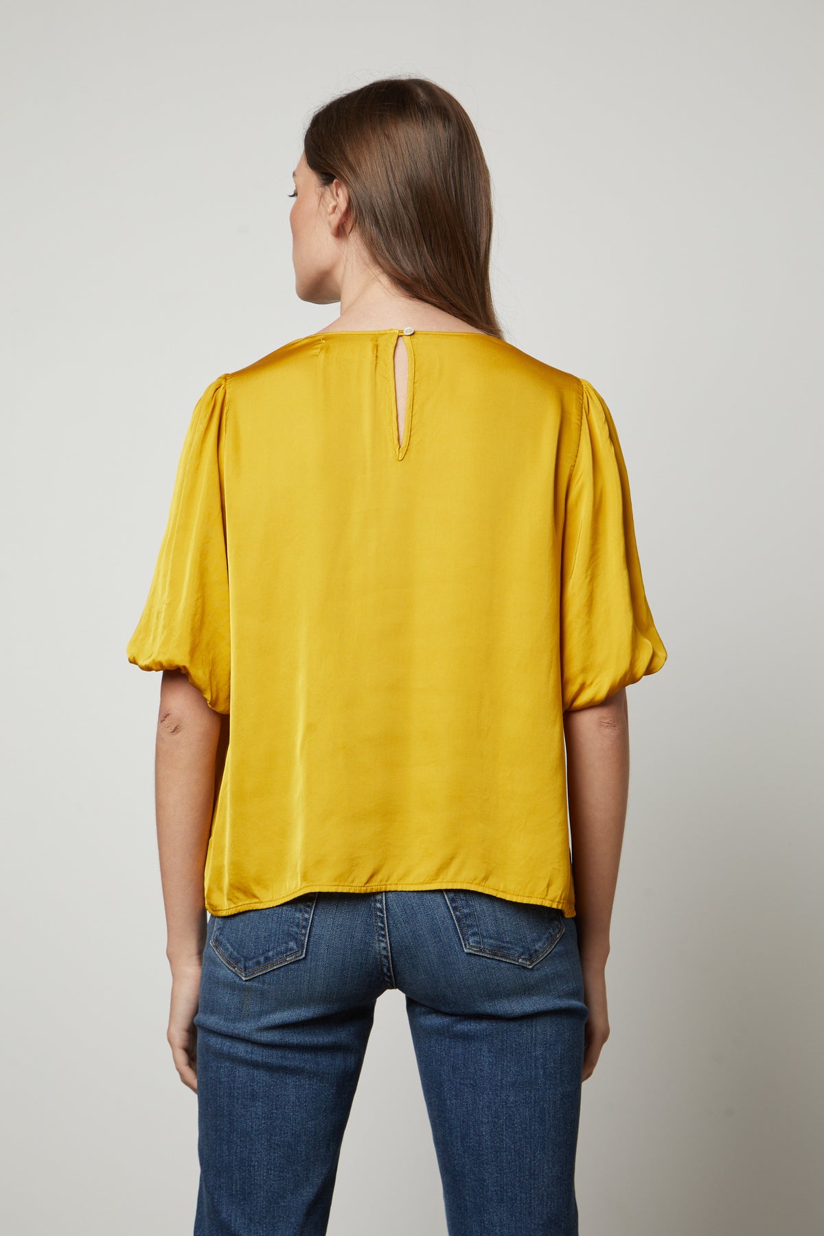 The back view of a woman wearing the Velvet by Graham & Spencer DESI SATIN PUFF SLEEVE TOP.-35656169488577