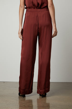 The woman is wearing a Velvet by Graham & Spencer burgundy jumpsuit with elastic waistline and slash pockets.