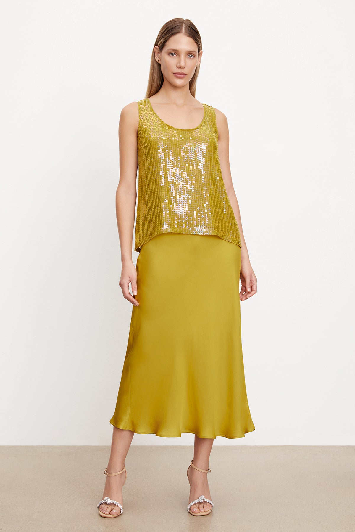   A woman wearing a yellow sequin top and Velvet by Graham & Spencer's AUBREE SATIN MIDI SKIRT in a silhouette. 