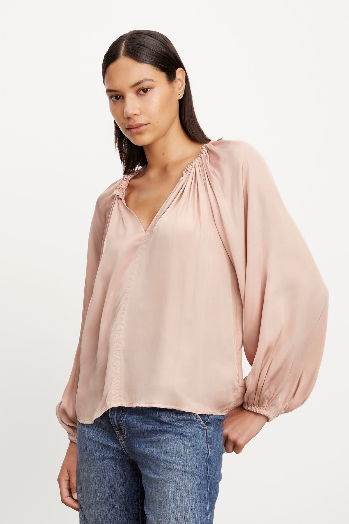   The model is wearing jeans and a NORIA SATIN PEASANT TOP by Velvet by Graham & Spencer, which has a relaxed fit and features a v-neckline. 