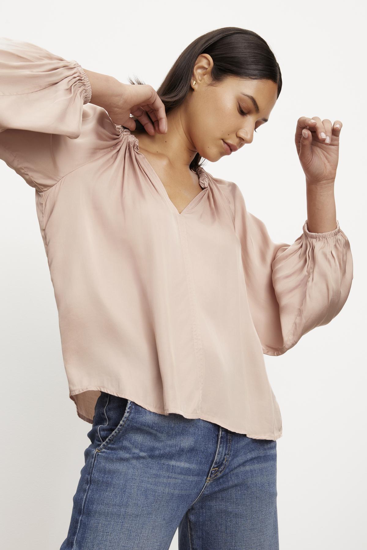 Woman adjusting a Velvet by Graham & Spencer Noria satin peasant top with a v-neckline while wearing blue jeans.-36328590082241