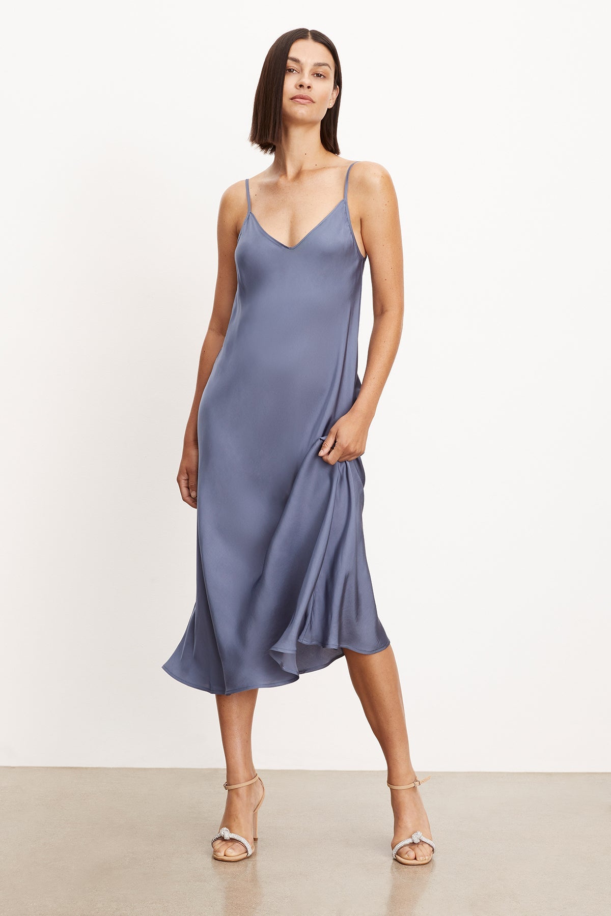 The model is wearing a blue Velvet by Graham & Spencer POPPY SATIN SLIP DRESS with adjustable straps, showcasing its versatility.-36001442070721