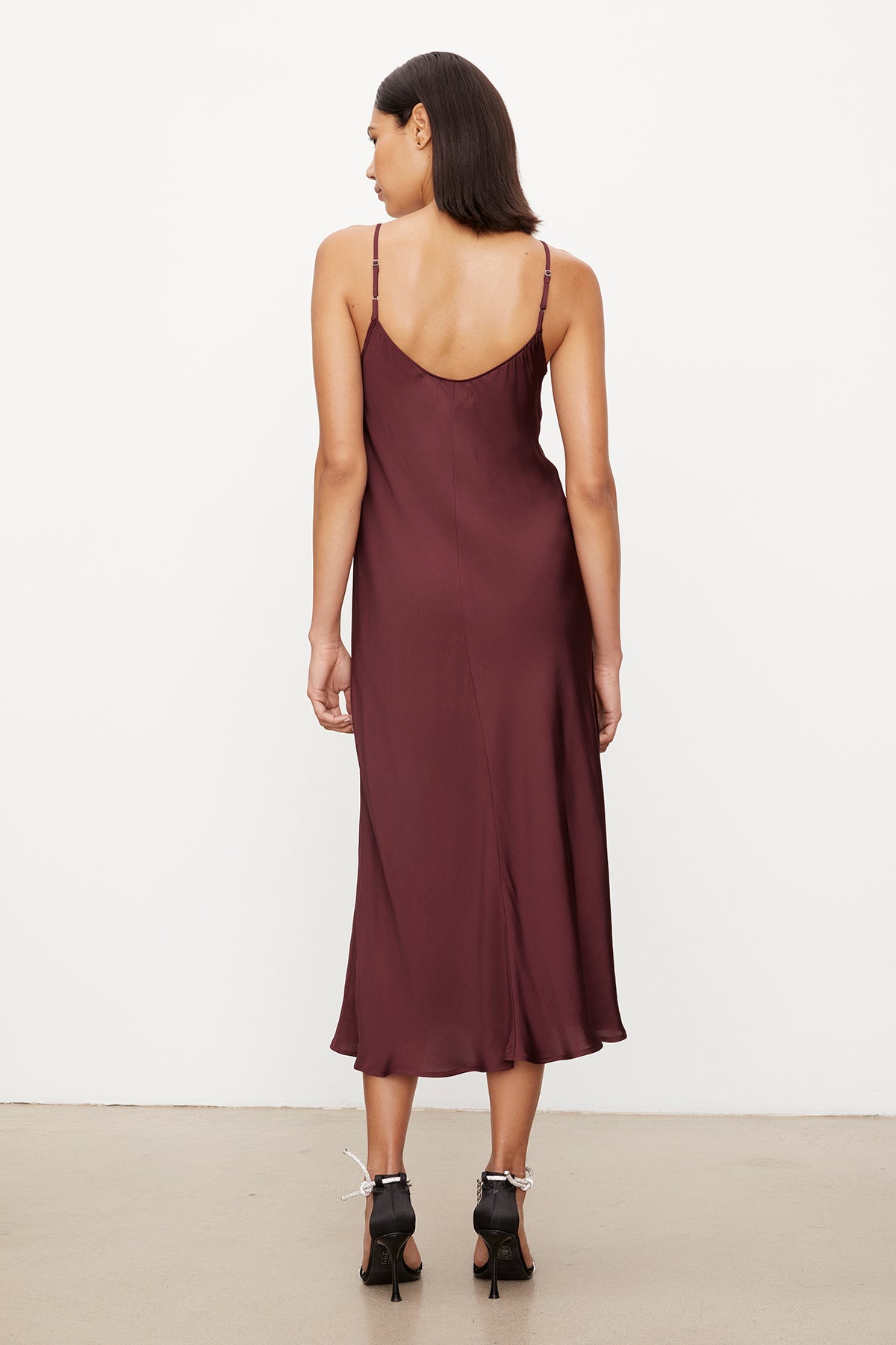 The versatile slip dress, the POPPY SATIN SLIP DRESS by Velvet by Graham & Spencer, features adjustable straps and showcases the back view of a woman wearing a burgundy slip dress.-35571939475649