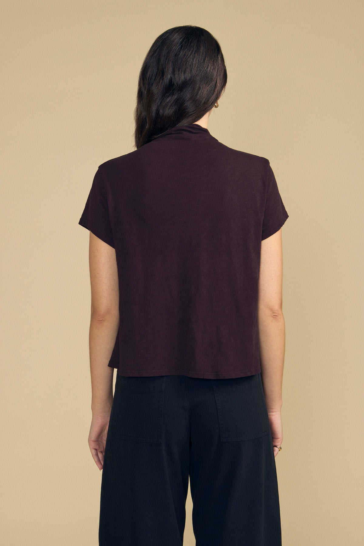 A person seen from the back wearing a dark brown, boxy silhouette SAVI TEE by Velvet by Graham & Spencer and black trousers.-46461710926017