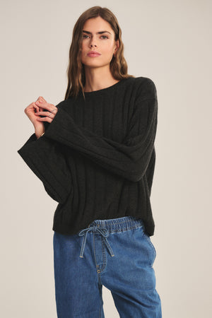 Model wears the SAWTELLE CASHMERE SWEATER by Velvet by Jenny Graham, a relaxed-fit black ribbed knit, paired with blue drawstring jeans against a simple light backdrop.
