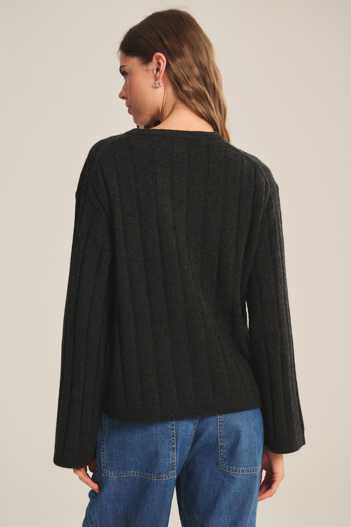 A woman faces away, wearing the SAWTELLE CASHMERE SWEATER by Velvet by Jenny Graham in ribbed black with blue jeans, set against a plain light background.-39838371643585