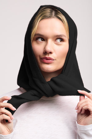 A woman wearing the LARGE TRIANGLE BANDANA BY 40 COLORI, a premium black headscarf by 40 Colori, and a white top looks slightly upward with a neutral expression.
