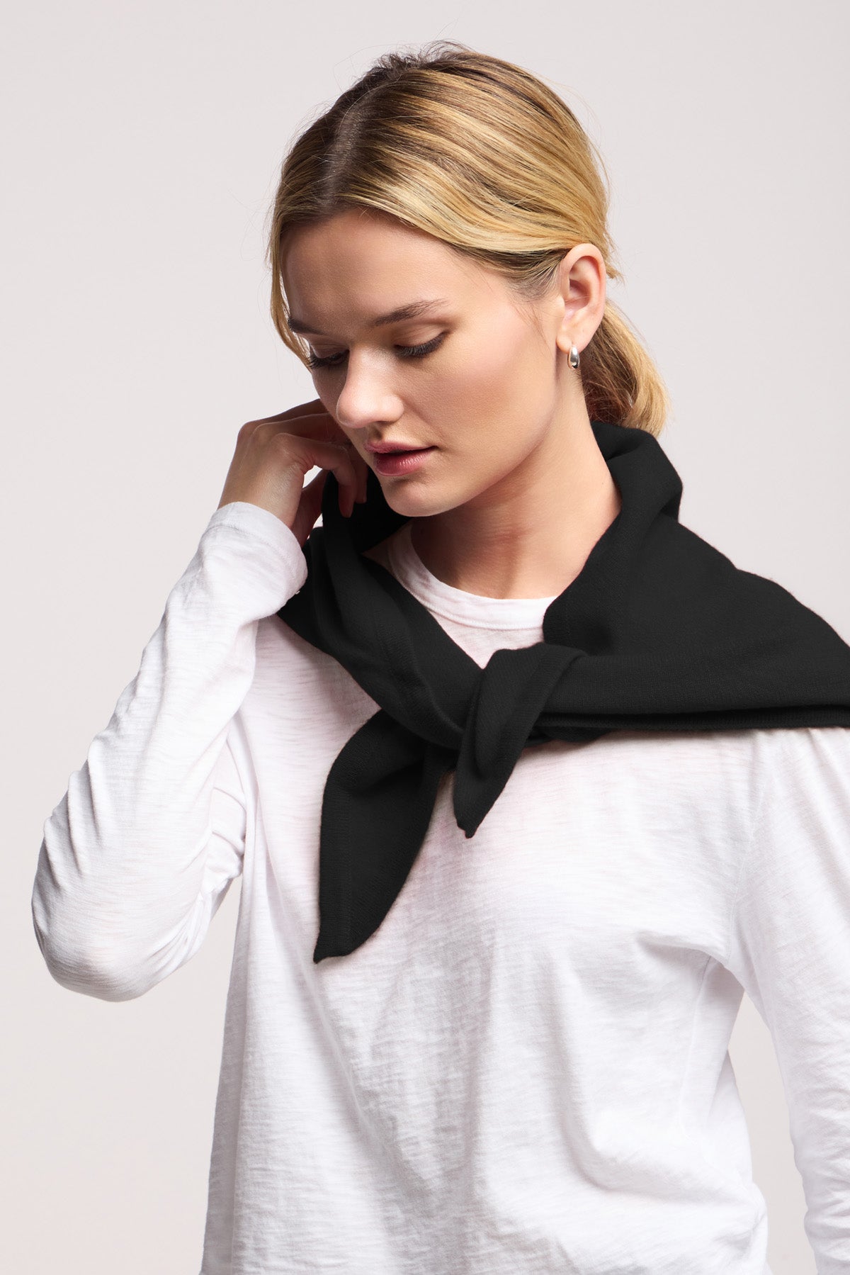 A woman wearing a white long-sleeve shirt with a black sweater draped over her shoulders, touching her neck, exudes elegance enhanced by the LARGE TRIANGLE BANDANA BY 40 COLORI from 40 Colori—perfect for channeling classic Italian style.