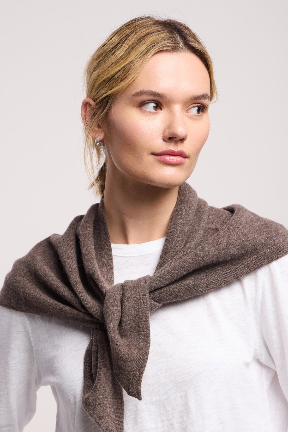 A woman with blonde hair in a low ponytail wears a white shirt and brown sweater, accented by the LARGE TRIANGLE BANDANA BY 40 COLORI tied at her neck as she looks slightly to the side.