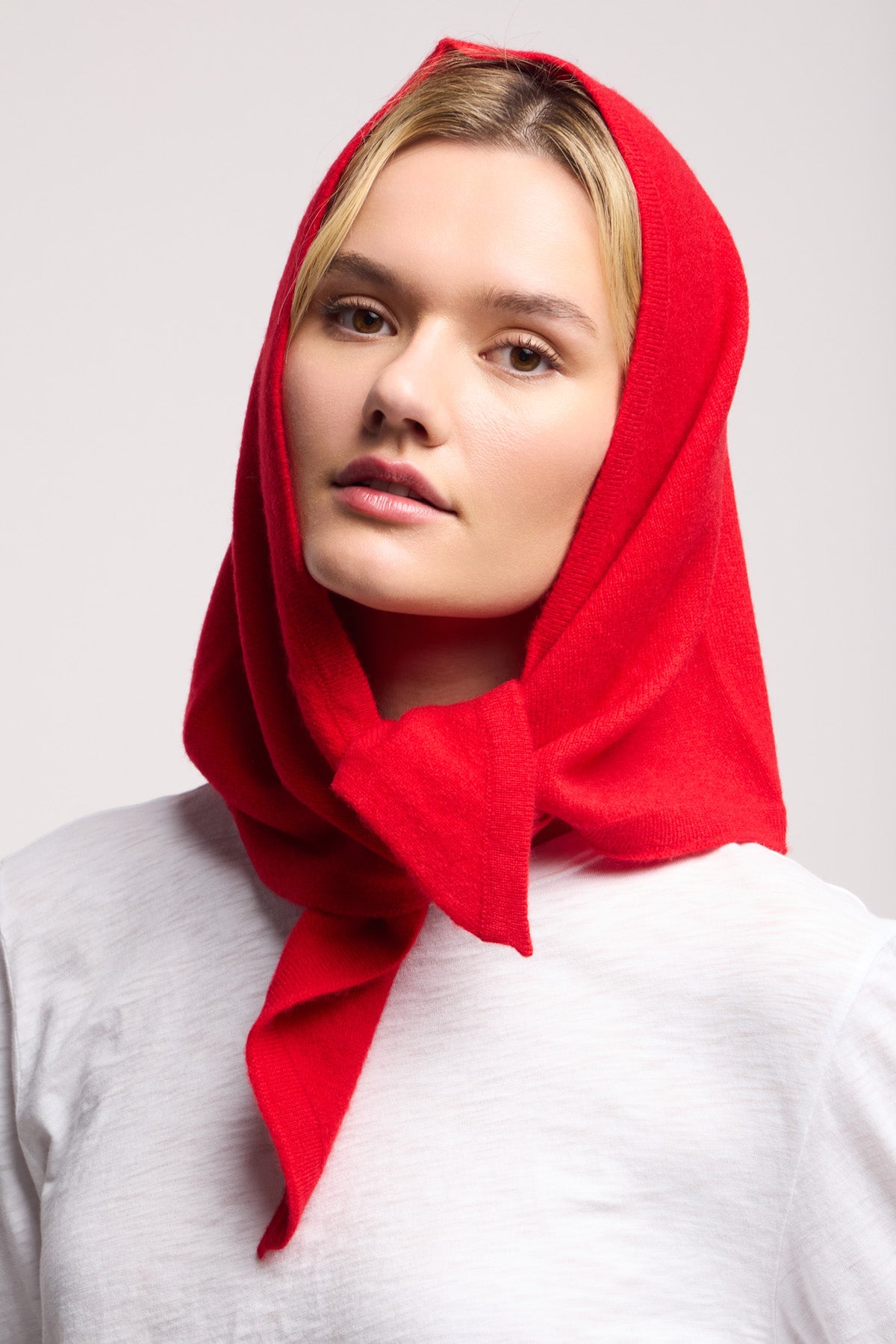 A woman wears a white shirt and the LARGE TRIANGLE BANDANA BY 40 COLORI, a premium red scarf by 40 Colori, wrapped around her head as she looks directly at the camera against a plain background.-40459576475841