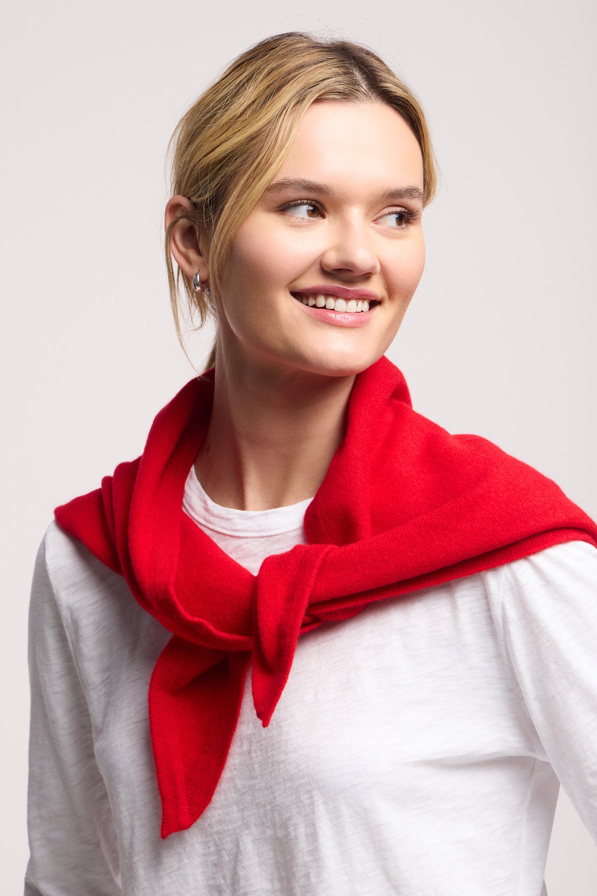 A young woman smiles and looks to the side against a plain background, effortlessly showcasing bold color and style with the LARGE TRIANGLE BANDANA BY 40 COLORI draped over her shoulders.