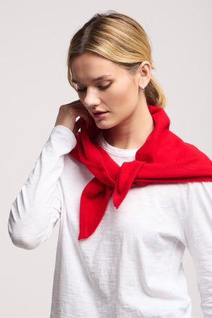 Woman wearing a white long-sleeve shirt and red sweater draped over her shoulders, looks down with her hand on her neck—her elegant look is finished with the LARGE TRIANGLE BANDANA BY 40 COLORI, a refined Italian accessory.