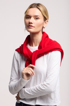 A woman with blonde hair stands against a plain background, wearing a white long-sleeve shirt with the LARGE TRIANGLE BANDANA BY 40 COLORI from 40 Colori in a bold red color draped over her shoulders.