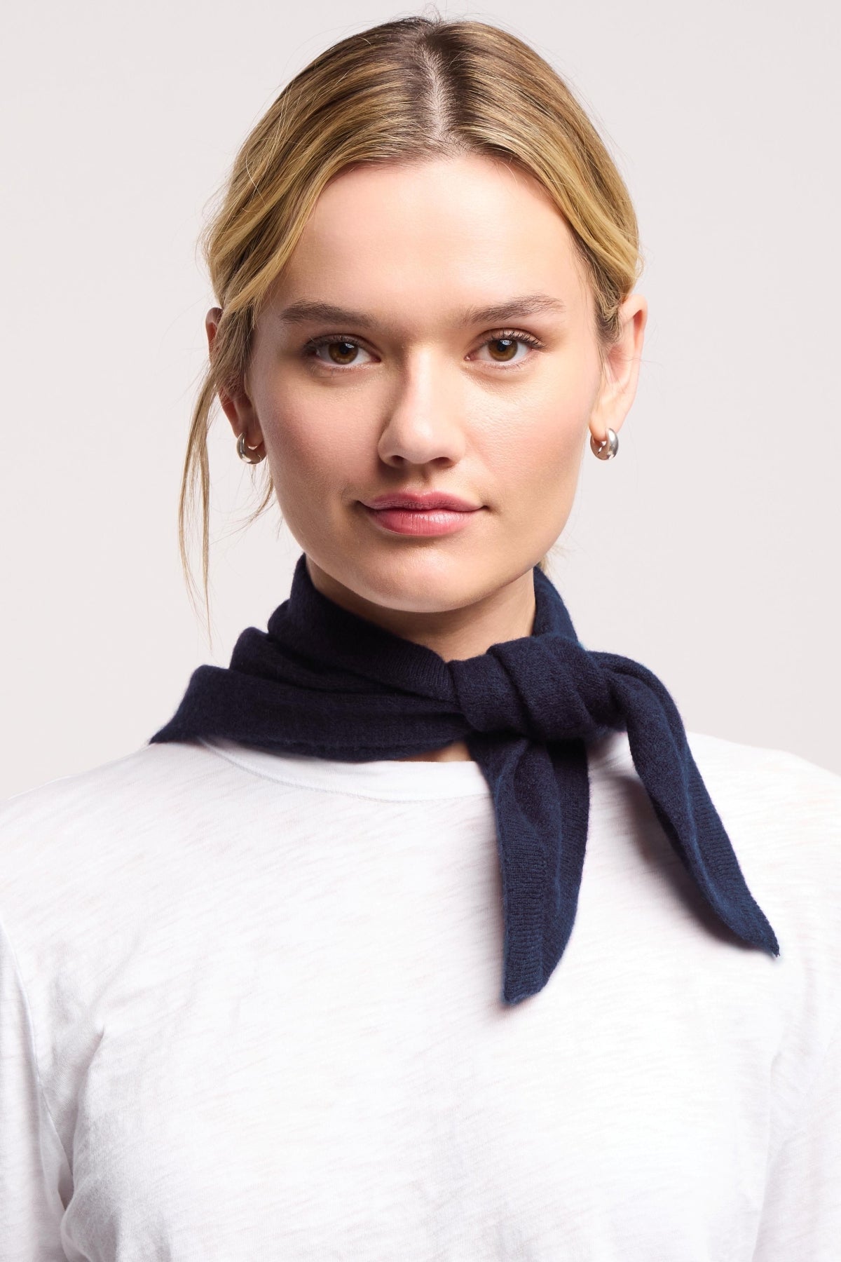 A person wearing a white shirt and the SMALL TRIANGLE BANDANA BY 40 COLORI from 40 Colori, tied around their neck, faces the camera against a plain background.