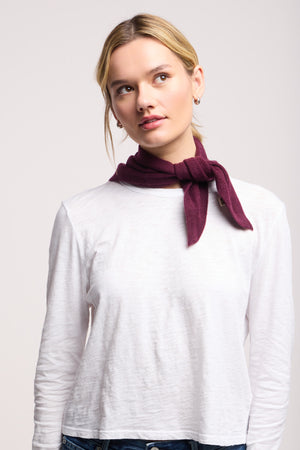 A woman wearing a white long-sleeve shirt and the 40 Colori Small Triangle Bandana, styled as a burgundy neck scarf, looks slightly upward to her left against a plain light background.