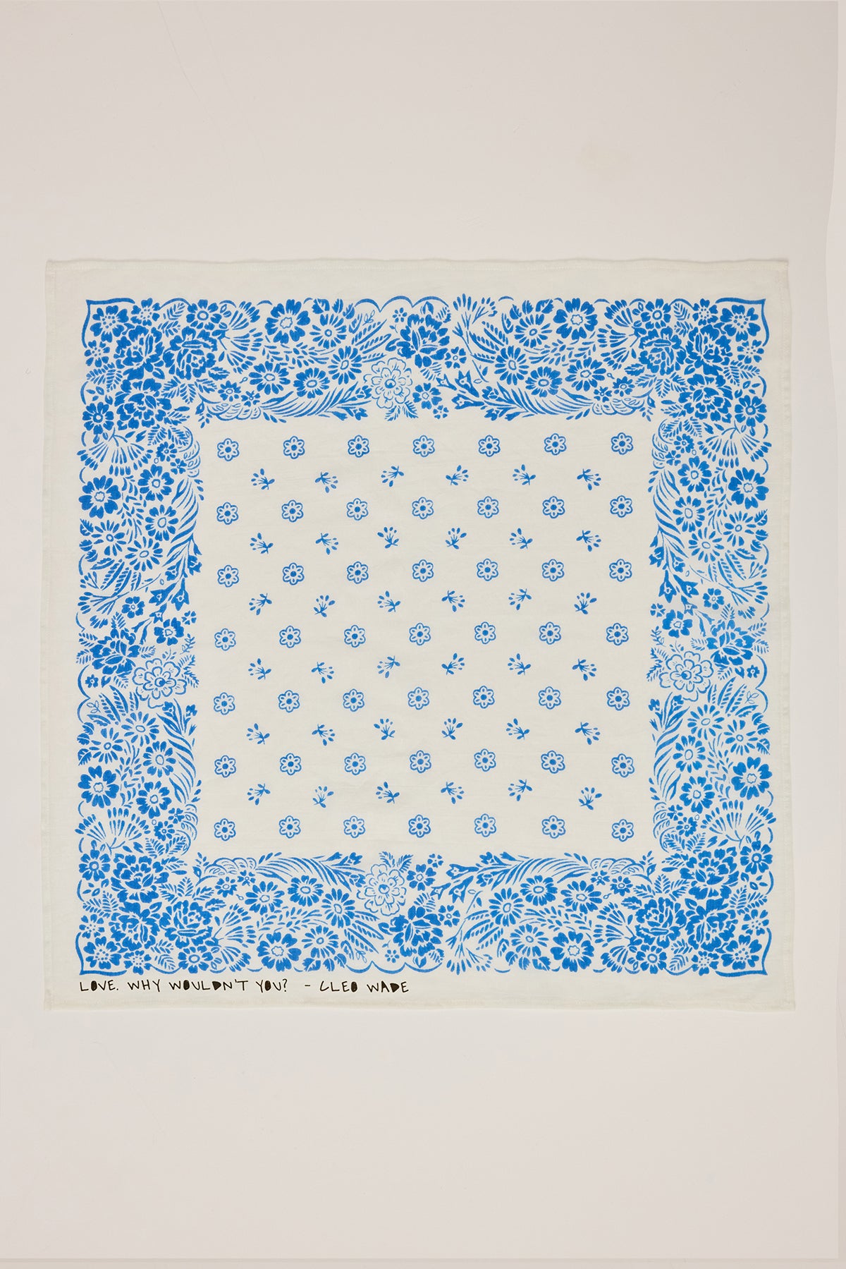 The NOLA SCARF by Velvet by Graham & Spencer is a white handkerchief made from lightweight woven cotton, featuring intricate blue floral and leaf patterns, with "LOVE, WHY WOULDN'T YOU? - CUCO VADE" at the bottom. Its versatile design echoes the poetic charm of Cleo Wade's work.-38864648929473