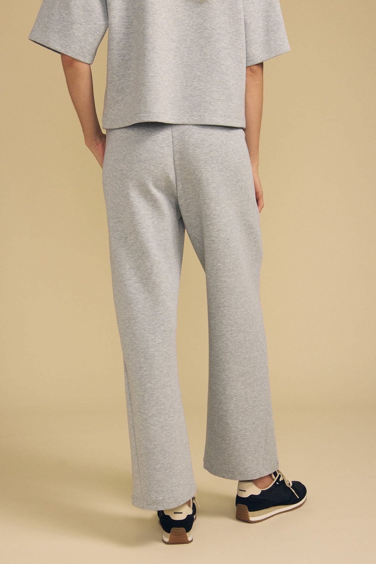 A person wearing the ARA SWEATPANT by Velvet by Graham & Spencer—a light gray, wide-leg pant—stands against a beige background, facing away.-41813597978817