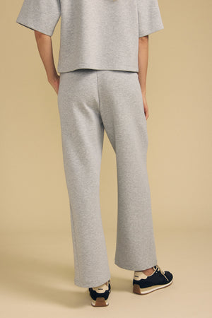 A person wearing the ARA SWEATPANT by Velvet by Graham & Spencer—a light gray, wide-leg pant—stands against a beige background, facing away.