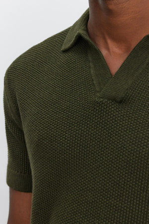 Close-up of a person wearing the NIKLAS SWEATER POLO by Velvet by Graham & Spencer, featuring a dark green color, short sleeves, textured knit fabric, a collar, and a V-neck.