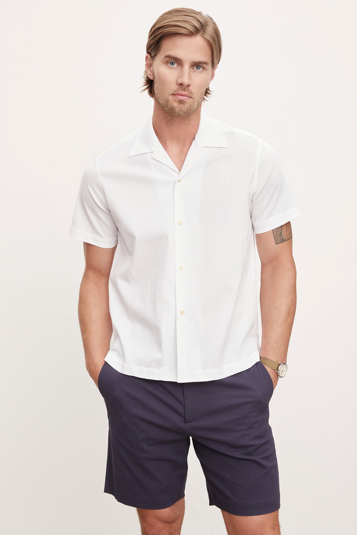 A man wearing a white Velvet by Graham & Spencer FRANK button-up shirt and navy shorts stands against a neutral background, looking at the camera.-36918598303937