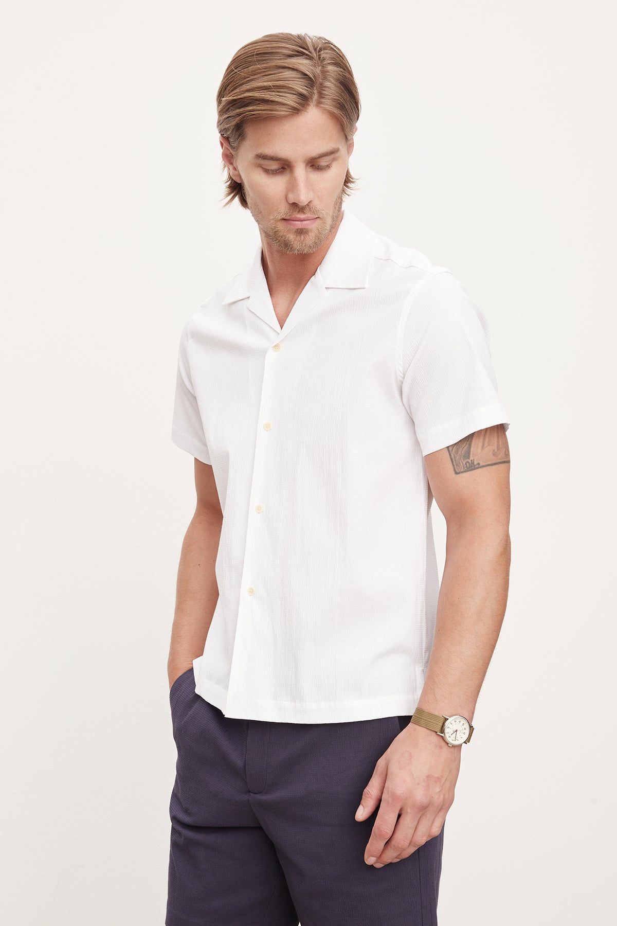 A man in a white short-sleeved Velvet by Graham & Spencer FRANK button-up shirt and dark pants, looking to the side with his hands in his pockets.-36918598336705