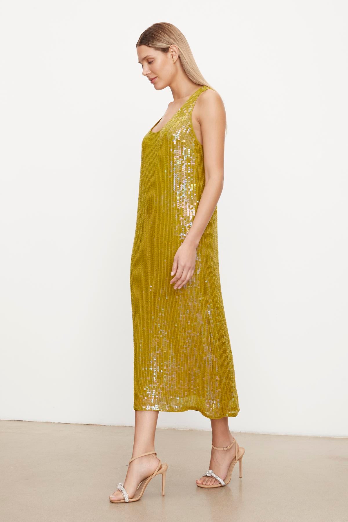   Woman in a yellow Velvet by Graham & Spencer ALENA SEQUIN TANK DRESS and beige heels standing against a plain background. 