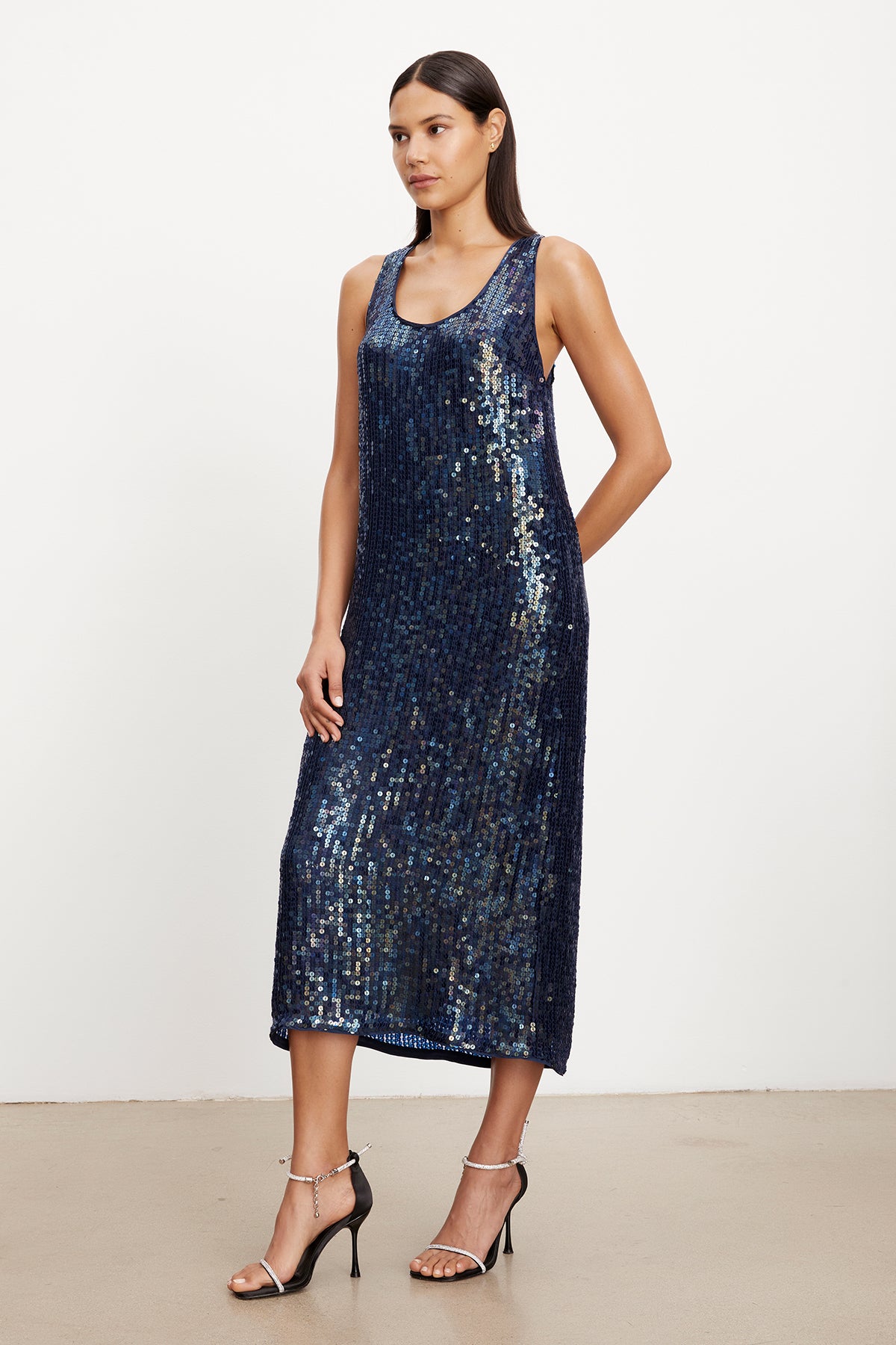 The elegance of the ALENA SEQUIN TANK DRESS shines through as the model confidently showcases her wardrobe in a stunning blue sequin midi dress by Velvet by Graham & Spencer.-35577745440961