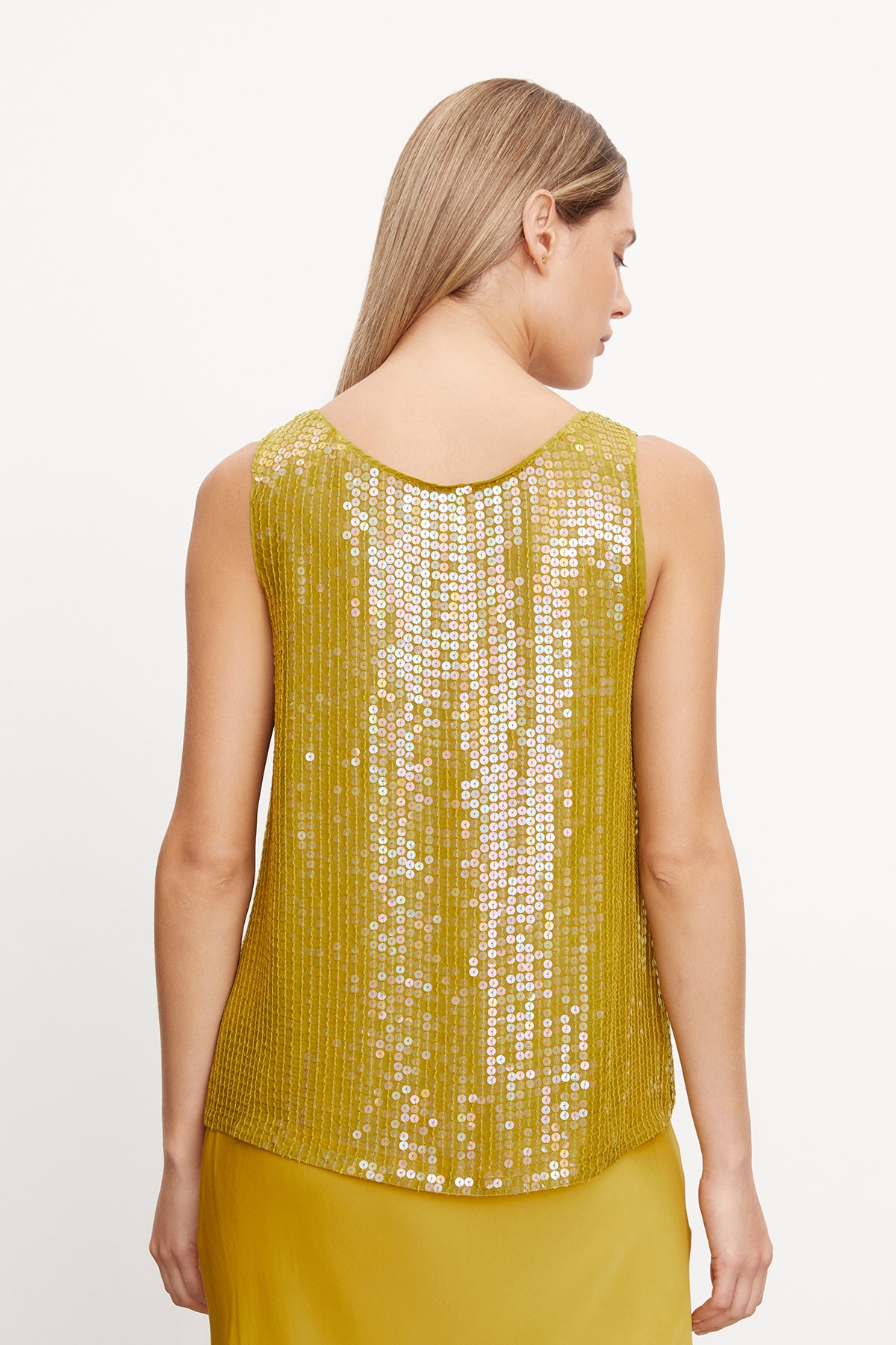   The woman is wearing a BEHATI SEQUIN TANK TOP by Velvet by Graham & Spencer, a yellow sequin top with chic scoop neckline and sequin detailing, showcasing an a-line silhouette from the back view. 