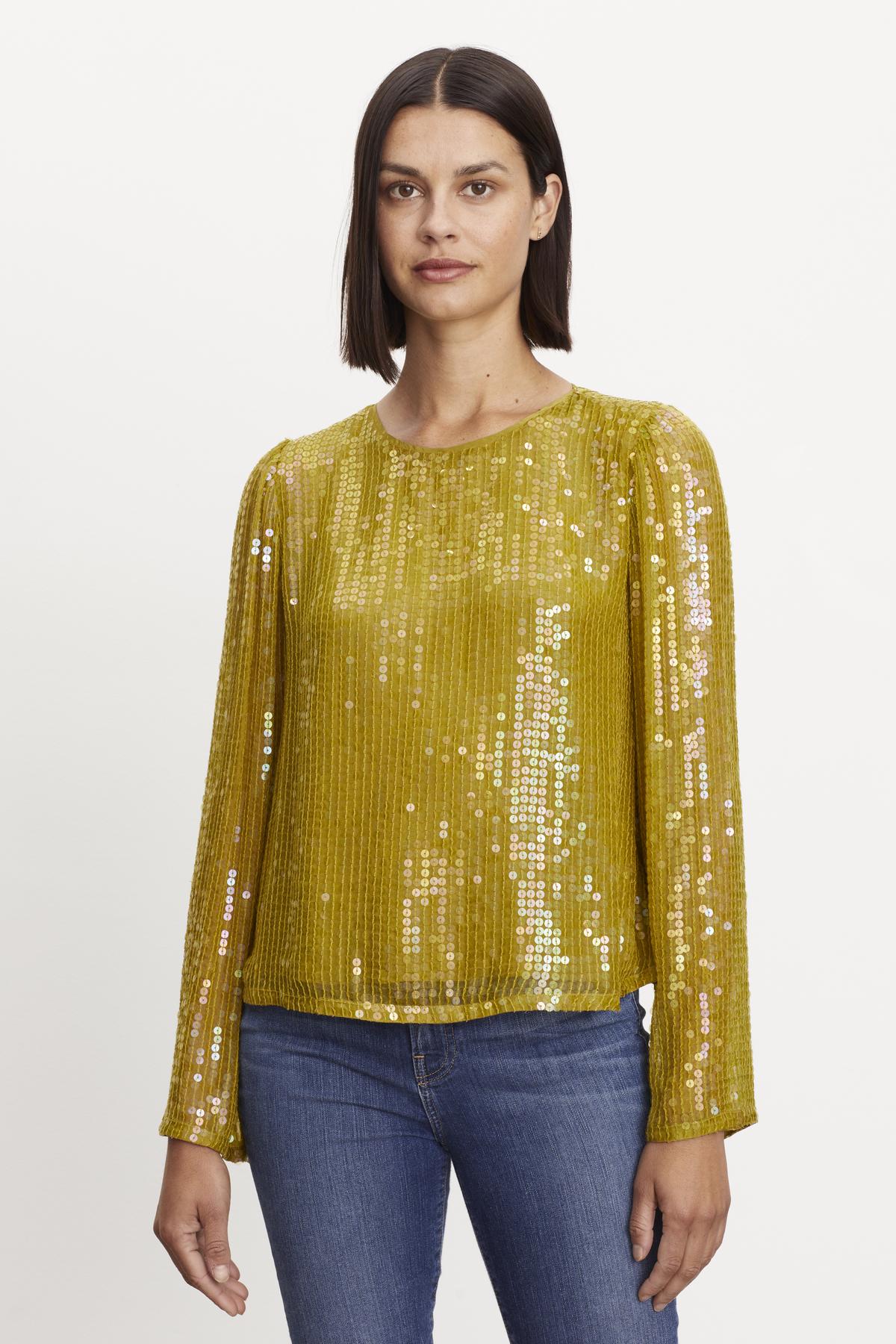 A woman is dressed in a modern twist on an evening ensemble, wearing a yellow Velvet by Graham & Spencer EVIE SEQUIN TOP and jeans.-36094468063425