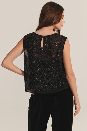A woman is shown from the back wearing the Velvet by Graham & Spencer SERENA TOP, a sleeveless black sequin evening top with a keyhole button closure, paired with black velvet pants.