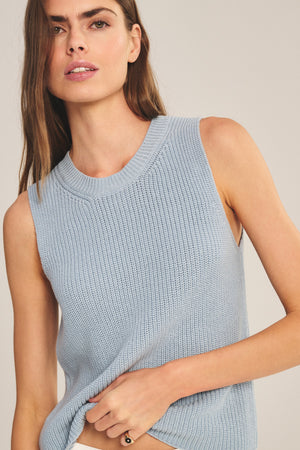 A woman models the Velvet by Graham & Spencer SERETTA SWEATER TANK, a sleeveless light blue Pima cotton top with a ribbed crew neckline, as she stands against a plain background, gazing slightly to the side.