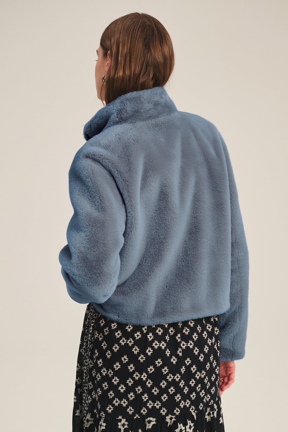 Model faces away from the camera, wearing the SHEENA LUXE FAUX FUR JACKET by Velvet by Graham & Spencer in light blue and a black skirt with white geometric print—a cozy, stylish look for chilly days.-39839681118401