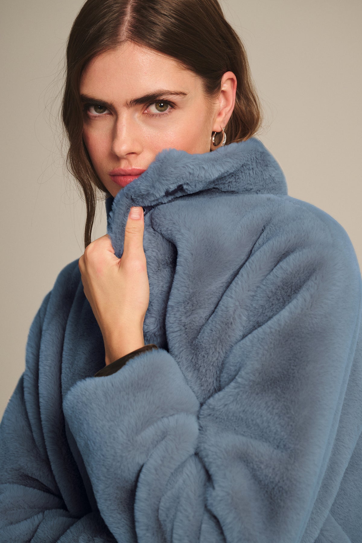 Model in the SHEENA LUXE FAUX FUR JACKET by Velvet by Graham & Spencer, light blue, cozy fit, holding the collar up near her face against a neutral background.-39839681020097