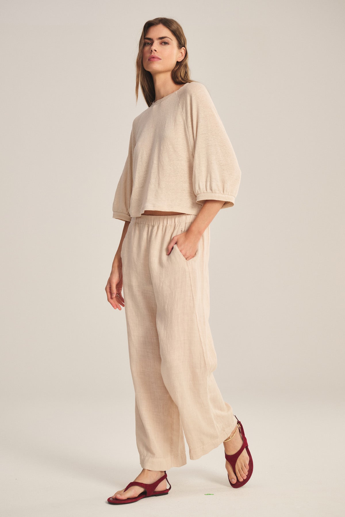 A person wears the LOLA LINEN PANT by Velvet by Graham & Spencer—loose-fitting, lightweight linen pull-ons with an elastic waist—paired with a beige three-quarter sleeve top and red sandals against a plain background.-40909840613569