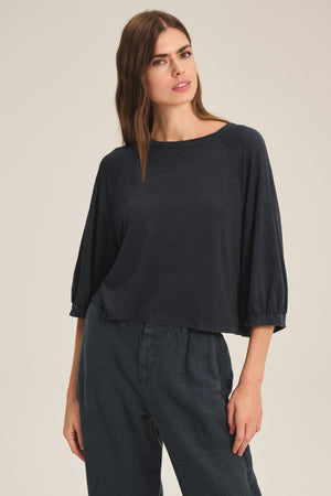 A woman wears the SHELLY TEE by Velvet by Graham & Spencer, a loose-fitting, dark, lightweight linen knit top paired with matching wide-leg pants, standing against a plain light background.