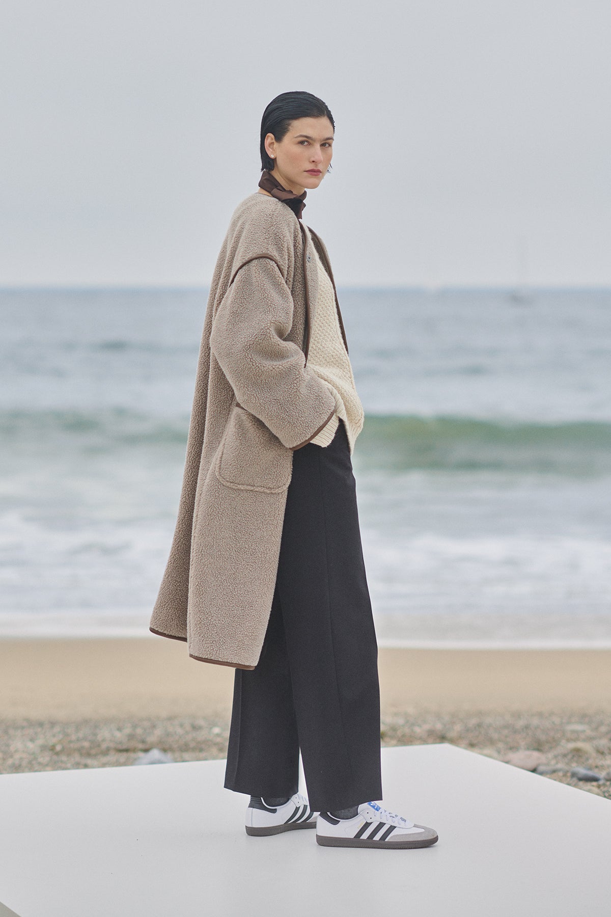 A woman in a Velvet by Jenny Graham Greenwich coat standing on the beach.-35547820916929