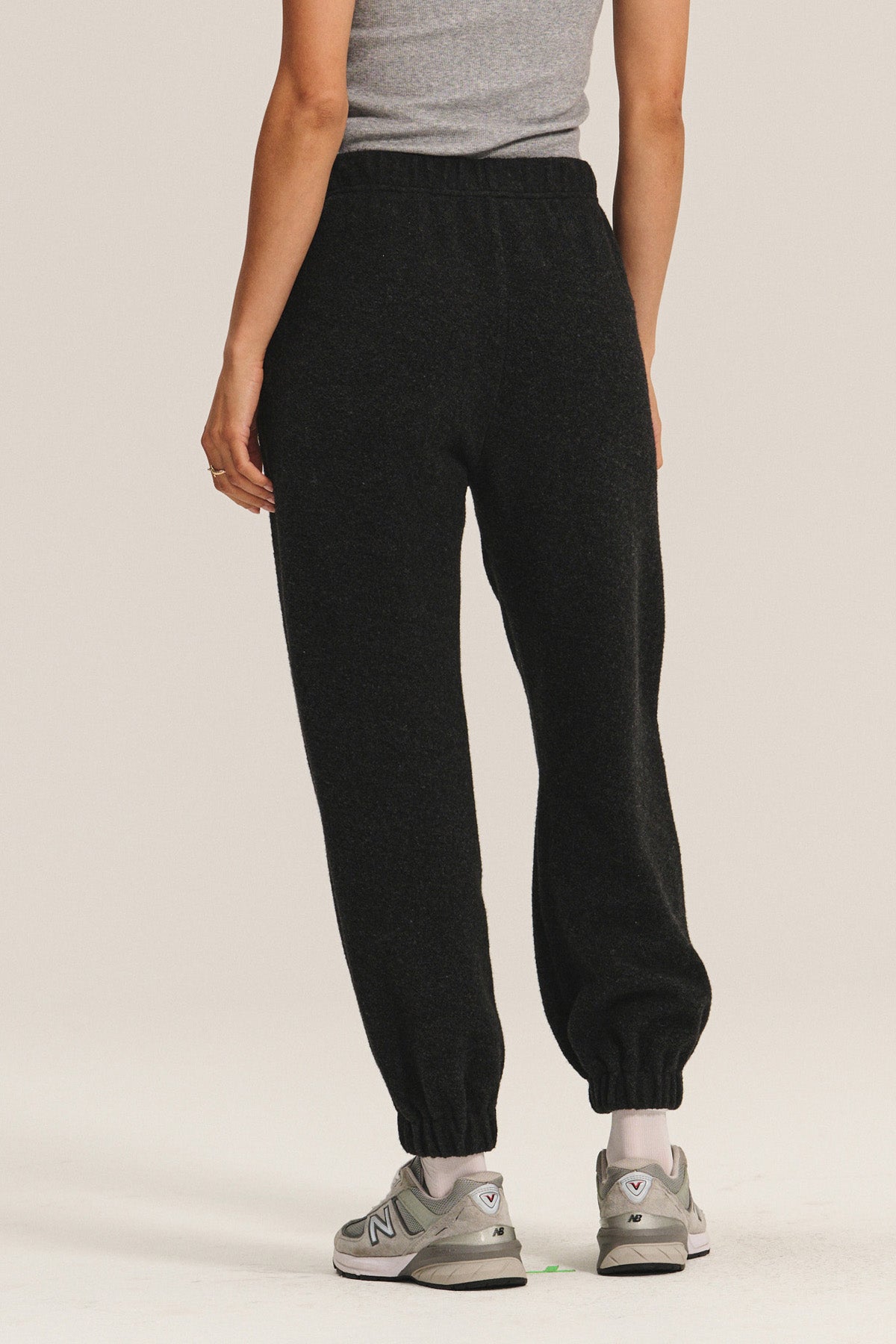A person wearing a grey sleeveless top, Velvet by Graham & Spencer DAWN JOGGER black sherpa fleece sweatpants with a pull-on fit, and grey sneakers is standing facing away from the camera.