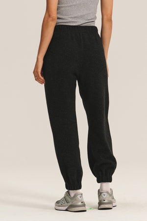 A person wearing a grey sleeveless top, Velvet by Graham & Spencer DAWN JOGGER black sherpa fleece sweatpants with a pull-on fit, and grey sneakers is standing facing away from the camera.