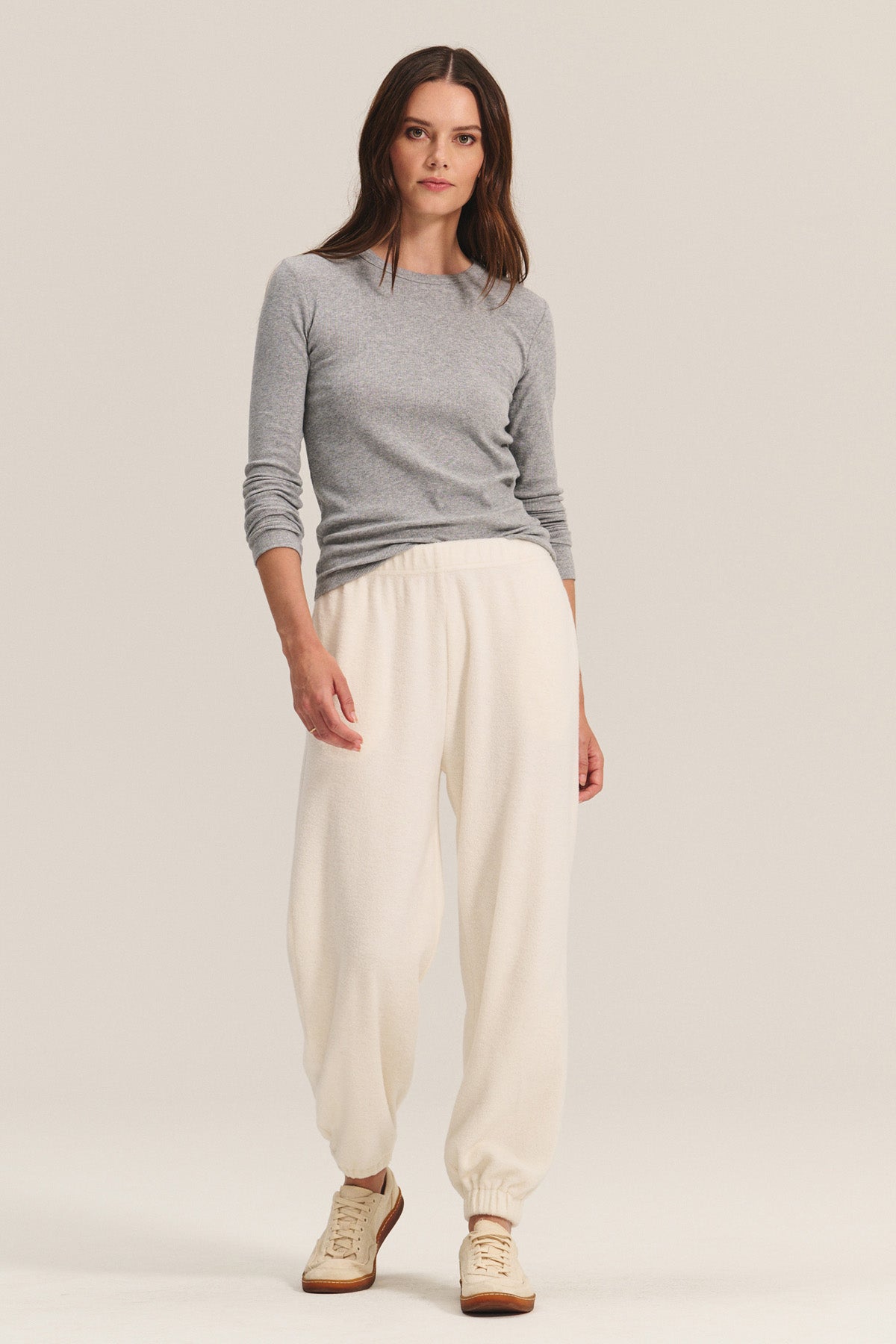 A woman stands against a neutral background wearing a grey long-sleeve top, Velvet by Graham & Spencer's DAWN JOGGER in cream sherpa fleece with a relaxed silhouette, and beige sneakers.-40334159577281