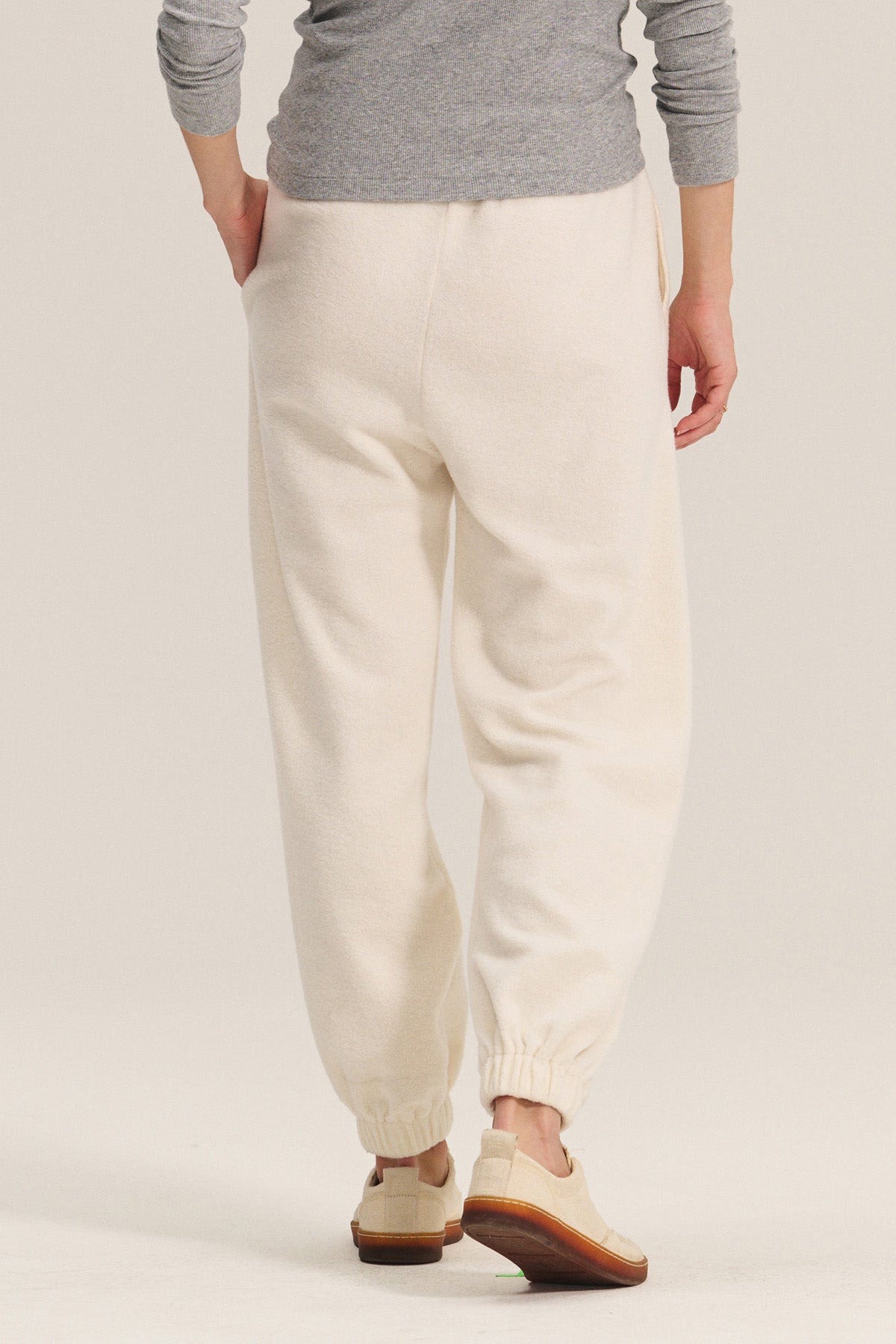 A person in Velvet by Graham & Spencer's DAWN JOGGER off-white sherpa fleece pants with a relaxed fit, paired with a grey long-sleeve top and beige shoes, stands facing away from the camera.